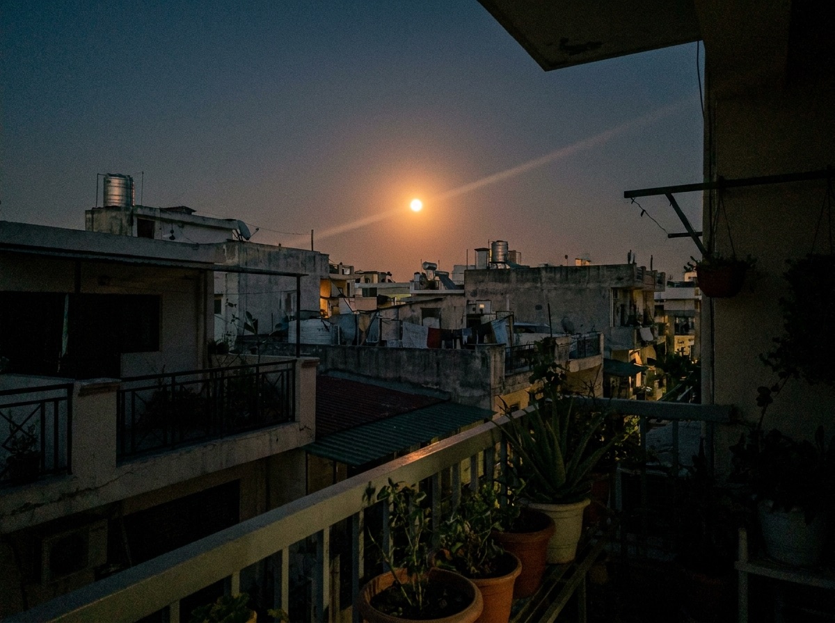 Moon above rooftops photographed from an apartment balcony